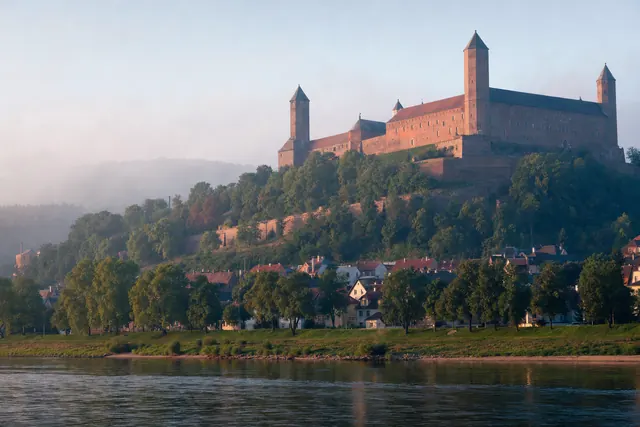 Castello in mattoni rossi con torri angolari sulla collina sopra il fiume Po (immagine creata con AI)